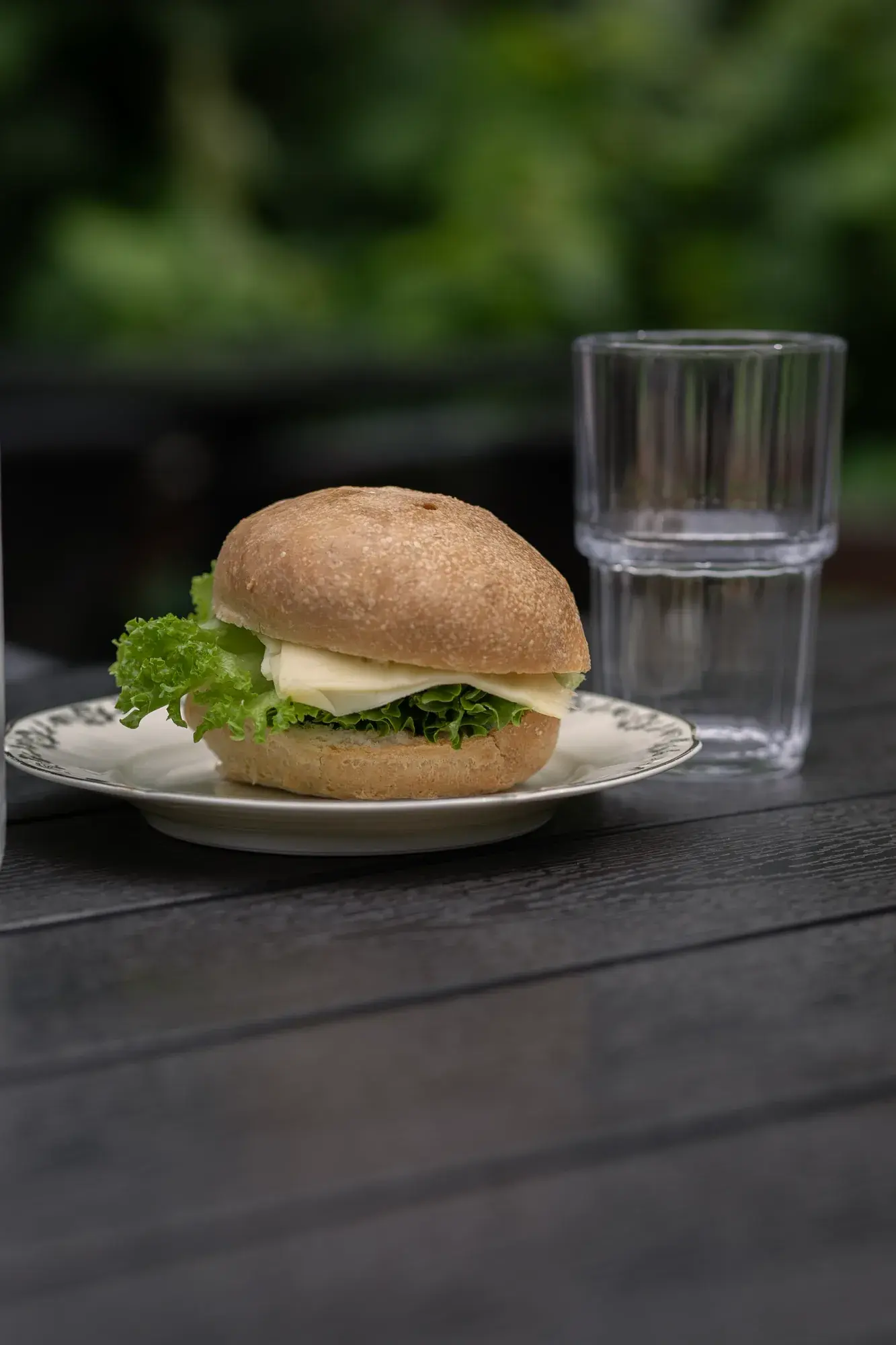 Fyllt bröd med sallad och ett glas vatten på ett bord utomhus