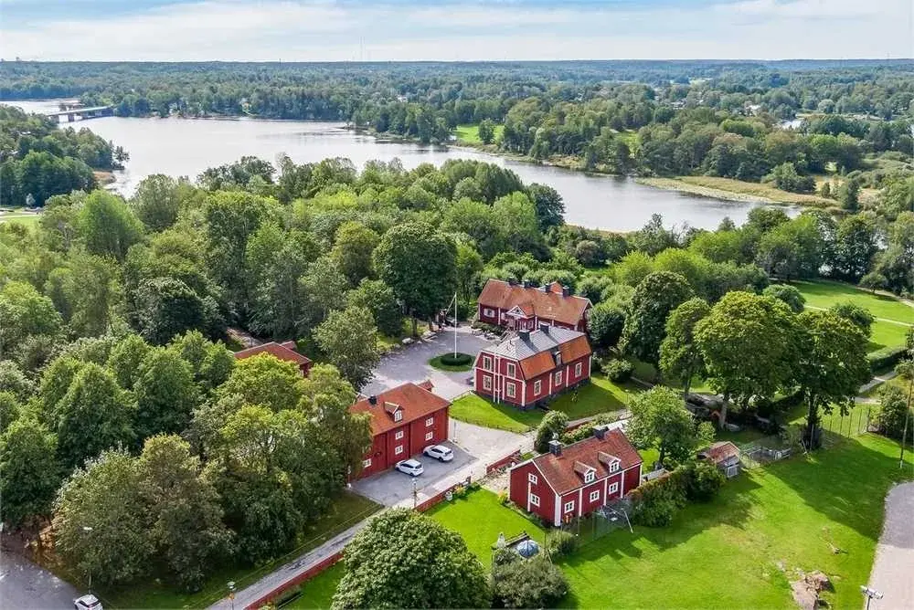 Farsta Gårds röda hus bland gröna träd och sjön intill